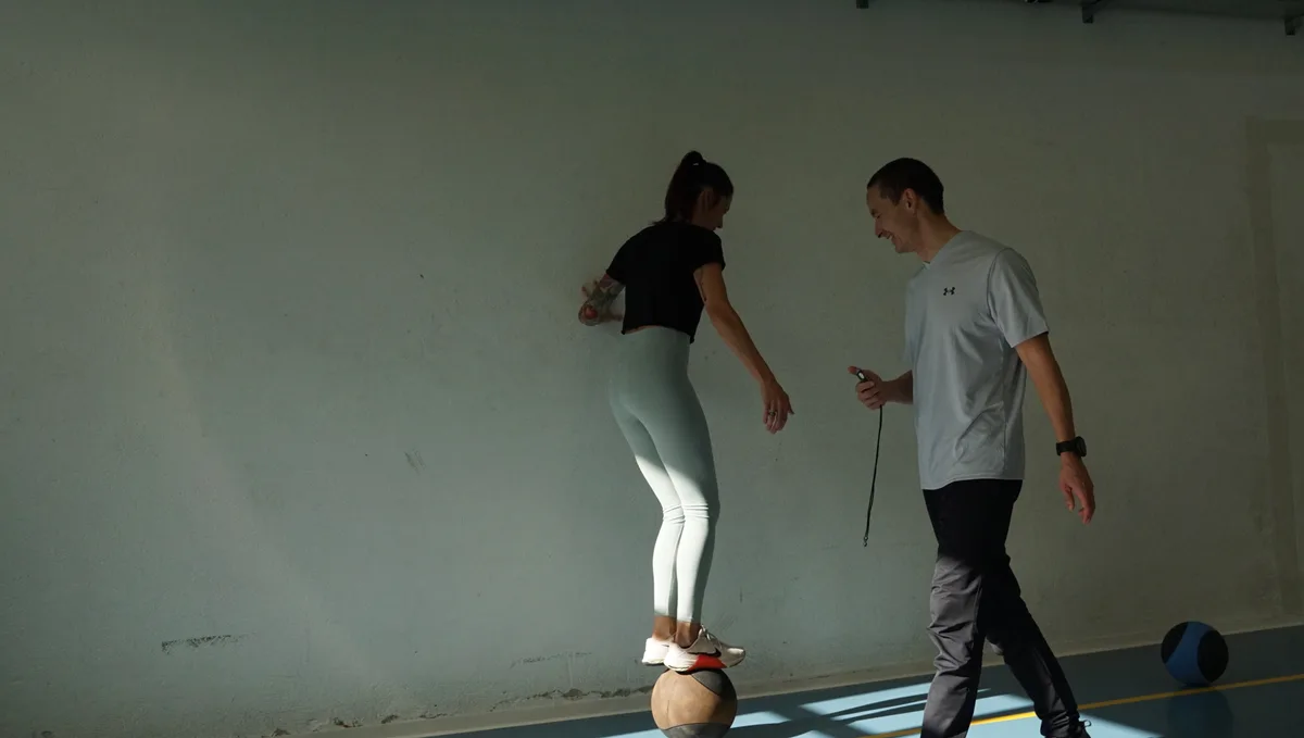 Man sieht eine Frau auf einem Ball und Lim, der zusieht. 